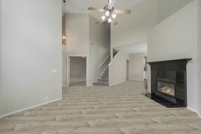 unfurnished living room featuring a tile fireplace, ceiling fan, high vaulted ceiling, and light hardwood / wood-style flooring