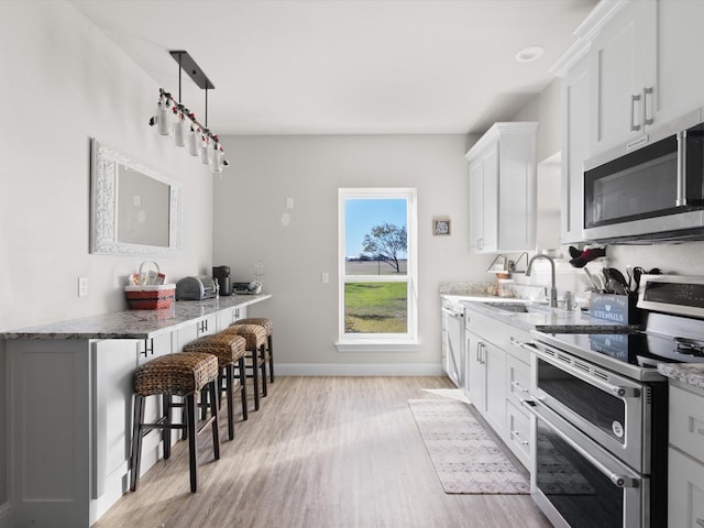 kitchen featuring appliances with stainless steel finishes, a kitchen breakfast bar, light stone counters, light hardwood / wood-style flooring, and white cabinets