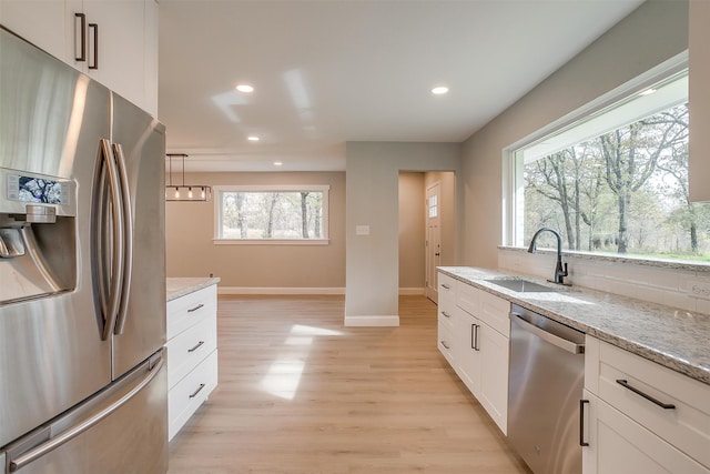 kitchen featuring light stone countertops, white cabinetry, sink, stainless steel appliances, and light wood-type flooring