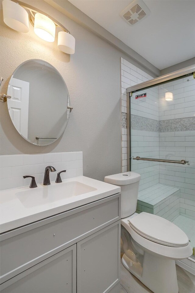 bathroom featuring vanity, toilet, an enclosed shower, and tasteful backsplash