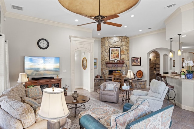 tiled living area with ceiling fan, a fireplace, visible vents, and crown molding