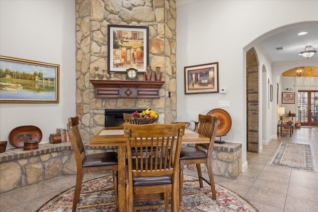 dining area featuring arched walkways, light tile patterned floors, visible vents, ornamental molding, and a stone fireplace