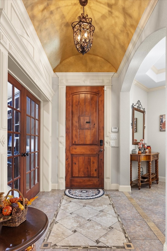 foyer entrance with a chandelier, vaulted ceiling, crown molding, and french doors