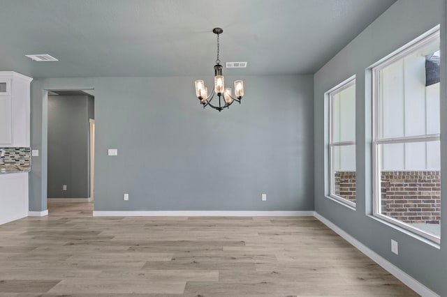 unfurnished dining area with an inviting chandelier and light hardwood / wood-style flooring