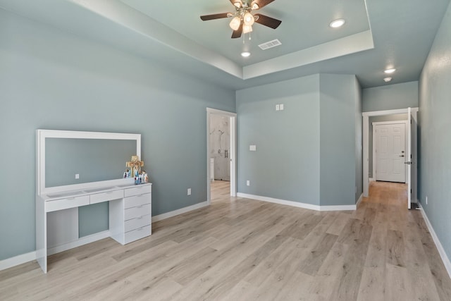 interior space featuring a raised ceiling, ceiling fan, and light wood-type flooring