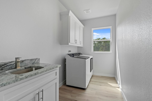 clothes washing area featuring washer and dryer, sink, cabinets, and light wood-type flooring