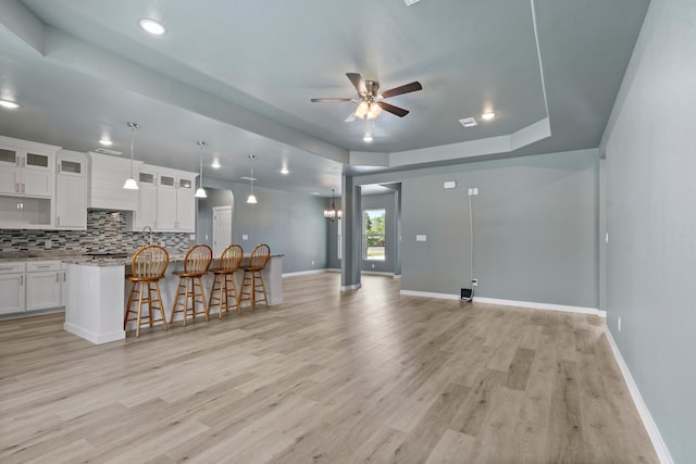 kitchen with light stone countertops, light wood-type flooring, a kitchen island, ceiling fan, and white cabinetry