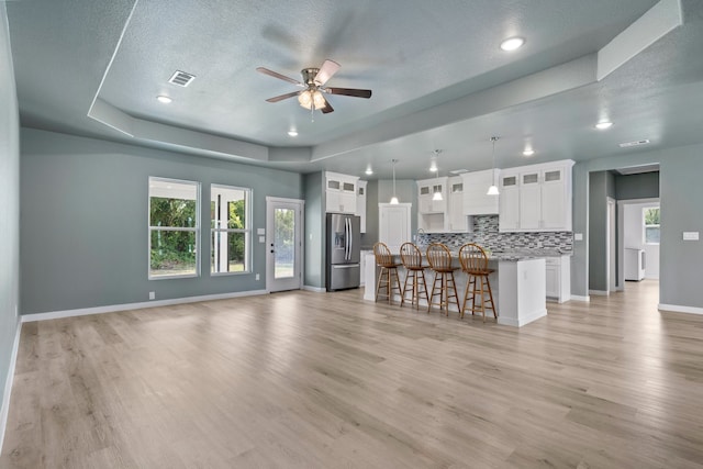 unfurnished living room featuring a textured ceiling, light wood-type flooring, a tray ceiling, and ceiling fan