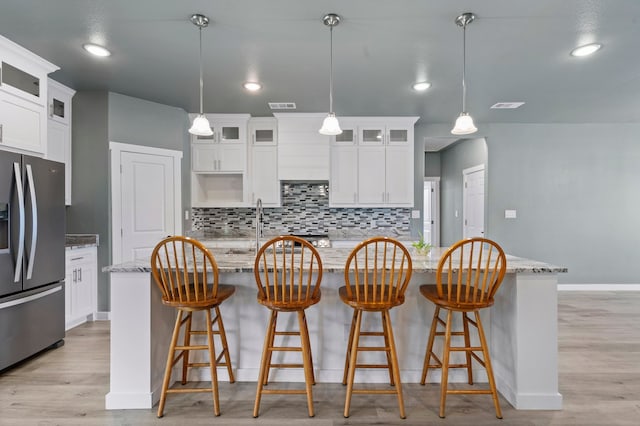 kitchen featuring hanging light fixtures, light stone countertops, a center island, and stainless steel refrigerator with ice dispenser