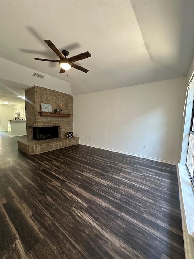 unfurnished living room featuring vaulted ceiling, dark hardwood / wood-style floors, ceiling fan, a brick fireplace, and a textured ceiling