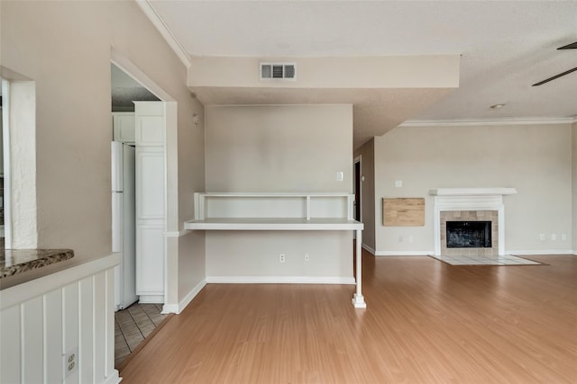 kitchen featuring a tile fireplace, white refrigerator, ornamental molding, a textured ceiling, and wood-type flooring