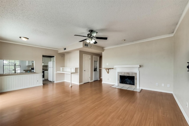 unfurnished living room featuring hardwood / wood-style floors, crown molding, a tile fireplace, and ceiling fan