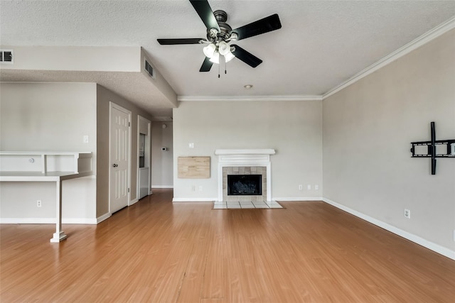 unfurnished living room with a tile fireplace, ceiling fan, crown molding, a textured ceiling, and hardwood / wood-style flooring