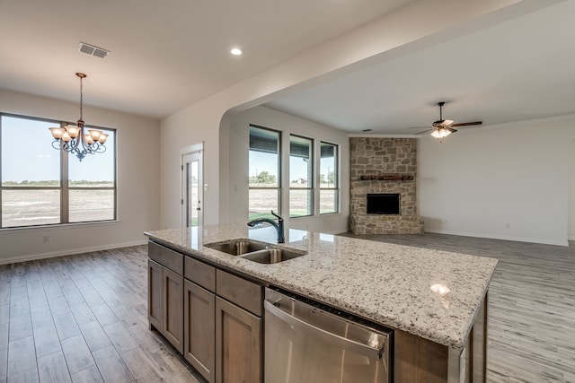 kitchen featuring stainless steel dishwasher, sink, pendant lighting, a fireplace, and an island with sink