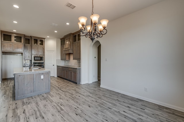 kitchen featuring appliances with stainless steel finishes, tasteful backsplash, light stone counters, a kitchen island with sink, and hanging light fixtures