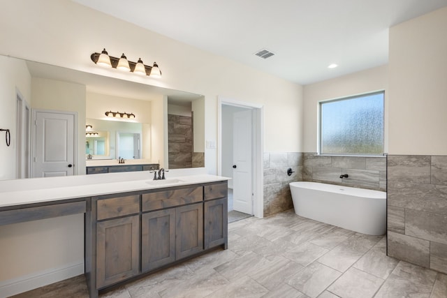 bathroom featuring vanity, a bath, and tile walls