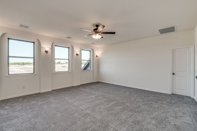 unfurnished room with a healthy amount of sunlight, ceiling fan, and dark carpet