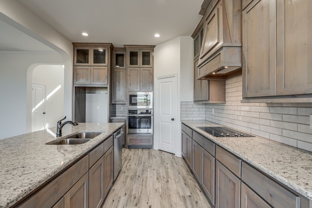 kitchen featuring light stone counters, custom range hood, sink, and appliances with stainless steel finishes