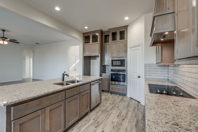 kitchen with sink, light wood-type flooring, appliances with stainless steel finishes, tasteful backsplash, and light stone counters