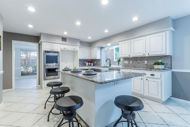 kitchen featuring a kitchen bar, a center island, dark stone countertops, stainless steel appliances, and white cabinets