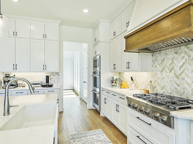 kitchen with stainless steel appliances, premium range hood, white cabinets, and light hardwood / wood-style flooring