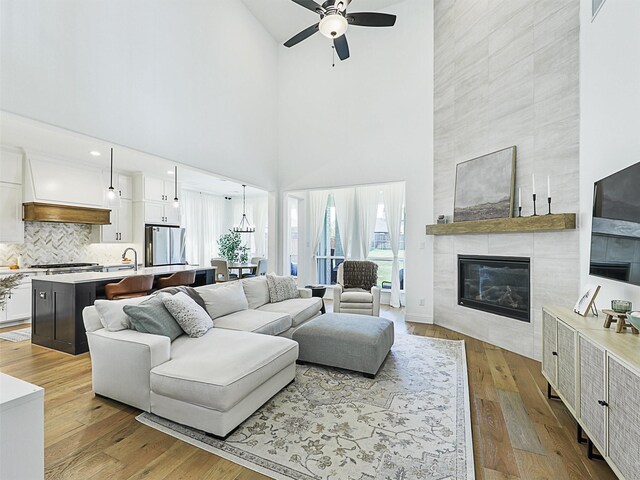 living room with light wood-type flooring, a towering ceiling, a fireplace, and ceiling fan