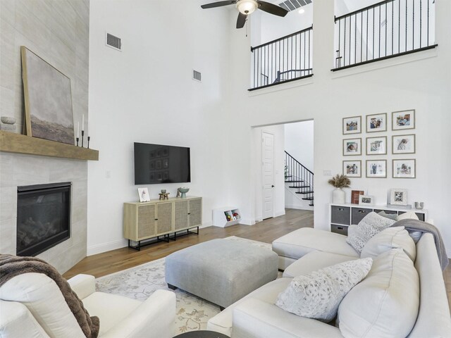 living room featuring hardwood / wood-style floors, ceiling fan, a tile fireplace, and a high ceiling