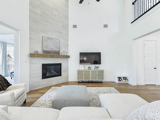 living room featuring wood-type flooring, a high ceiling, ceiling fan, and a tiled fireplace