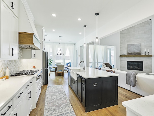 kitchen with a tile fireplace, light wood-type flooring, a kitchen island with sink, and hanging light fixtures