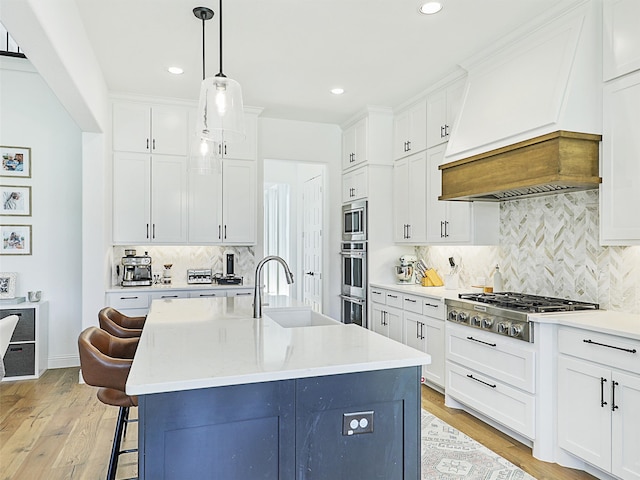 kitchen featuring stainless steel gas stovetop, premium range hood, sink, light hardwood / wood-style flooring, and an island with sink