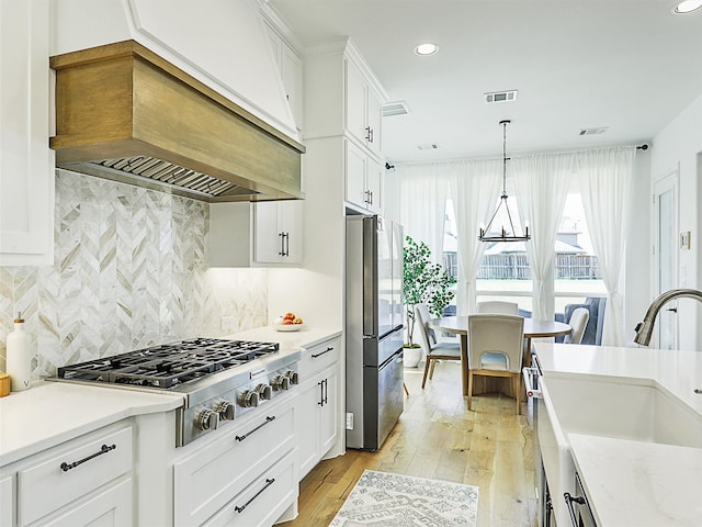 kitchen with white cabinetry, light wood-type flooring, premium range hood, and appliances with stainless steel finishes