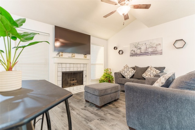 living room with ceiling fan, lofted ceiling, a tiled fireplace, and wood-type flooring