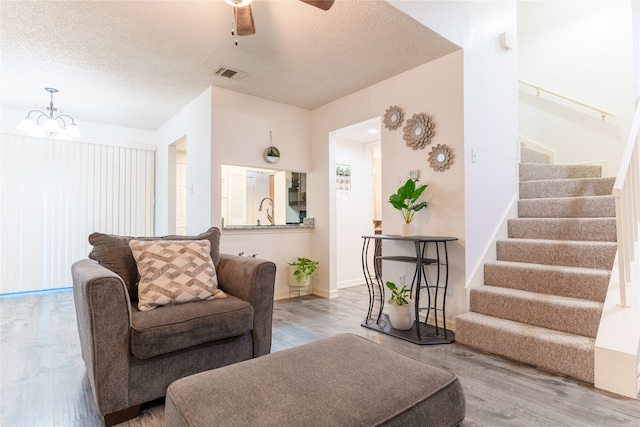 living room featuring hardwood / wood-style floors, ceiling fan with notable chandelier, sink, and a textured ceiling