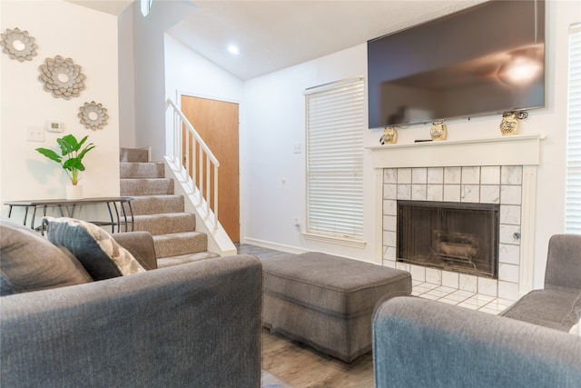 living room featuring a tile fireplace, light wood-type flooring, and vaulted ceiling