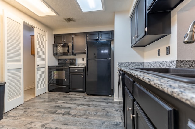 kitchen with light wood-type flooring, light stone counters, a textured ceiling, sink, and black appliances