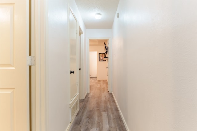 hall with light hardwood / wood-style floors and a textured ceiling