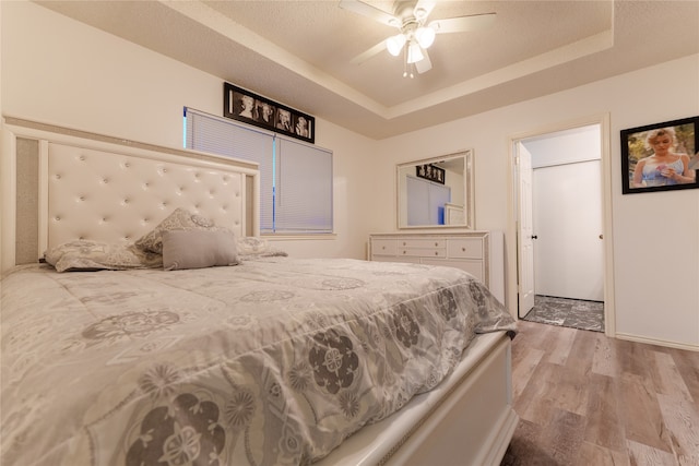 bedroom with light hardwood / wood-style floors, a raised ceiling, and ceiling fan