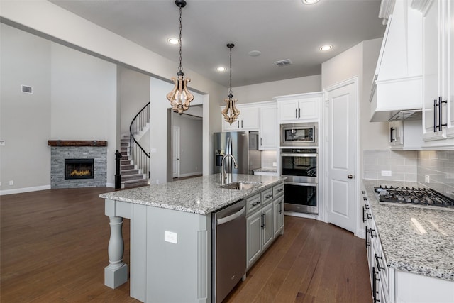 kitchen featuring white cabinetry, appliances with stainless steel finishes, a center island with sink, and a stone fireplace