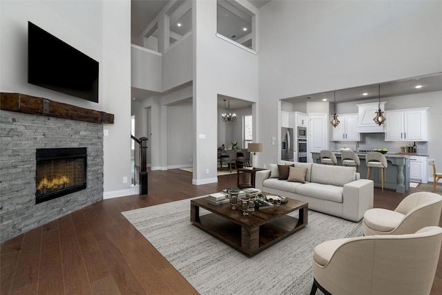 living room featuring a stone fireplace, a towering ceiling, an inviting chandelier, and dark hardwood / wood-style floors