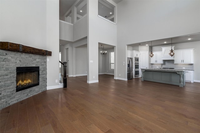 unfurnished living room featuring a high ceiling, a stone fireplace, and dark hardwood / wood-style flooring