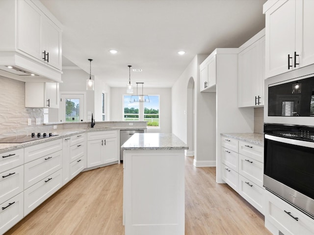 kitchen with appliances with stainless steel finishes, a kitchen island, sink, white cabinetry, and hanging light fixtures