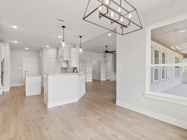 kitchen featuring ceiling fan, decorative light fixtures, a center island with sink, white cabinets, and light hardwood / wood-style floors