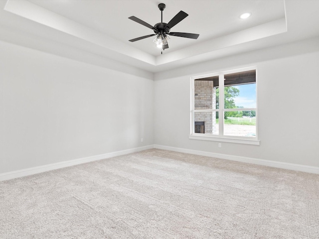 carpeted spare room featuring a tray ceiling and ceiling fan