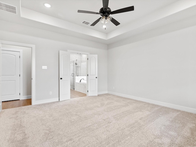 unfurnished bedroom with a raised ceiling, ensuite bath, ceiling fan, and light carpet