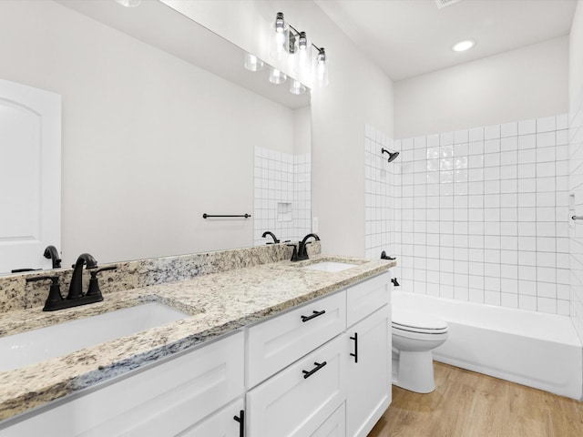 full bathroom featuring hardwood / wood-style floors, vanity, tiled shower / bath combo, and toilet