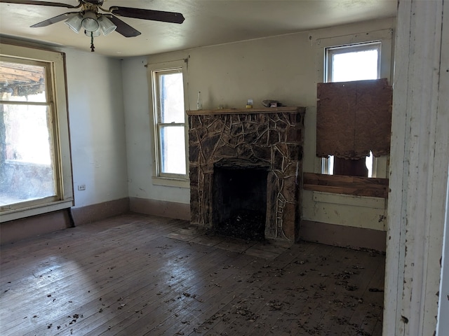 unfurnished living room with ceiling fan, a stone fireplace, and wood-type flooring