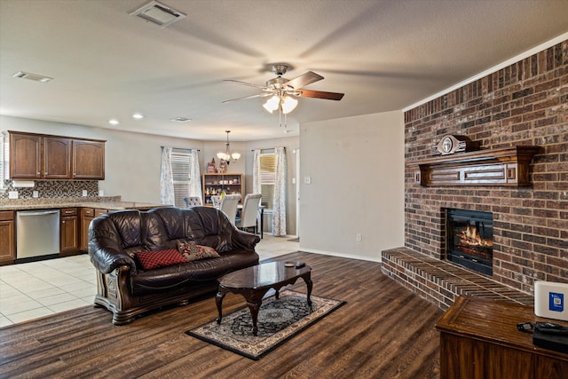 living room with a brick fireplace, ceiling fan with notable chandelier, a textured ceiling, and light hardwood / wood-style flooring