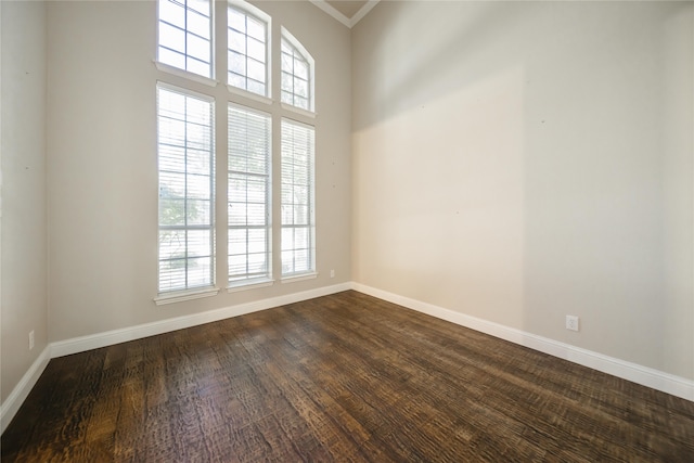 unfurnished room with a towering ceiling, ornamental molding, dark hardwood / wood-style flooring, and a healthy amount of sunlight