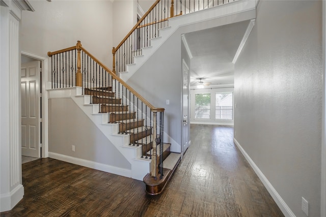 stairway featuring wood-type flooring, a towering ceiling, and ornamental molding