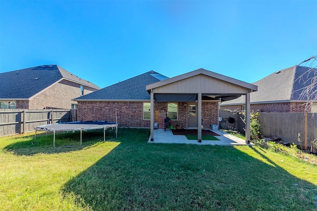 back of property featuring a trampoline, a patio area, and a lawn